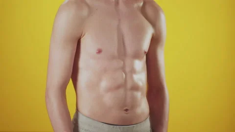 Athletic man poses on yellow background in studio, closeup off abs, front view Stock Footage 163872615