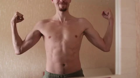 Athletic man posing in front of a mirror. A man looking at the muscles of the Stock Footage 265017650