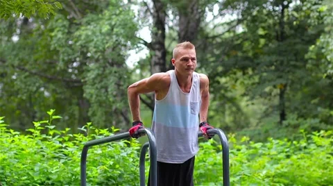 Athletic man is pushed on bars in City Park under summer trees for sport fitness Stock-Footage 66420637