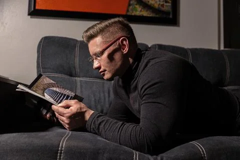 Athletic man reading a book on a sofa in a cozy indoor setting during evening Stock Photos