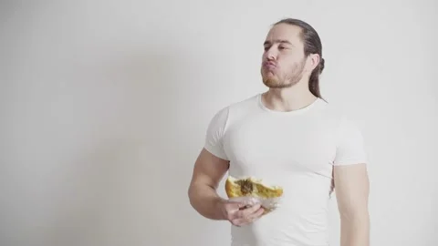 Athletic man with a red beard, in a white T-shirt on a white background, eats Stock Footage 131057446