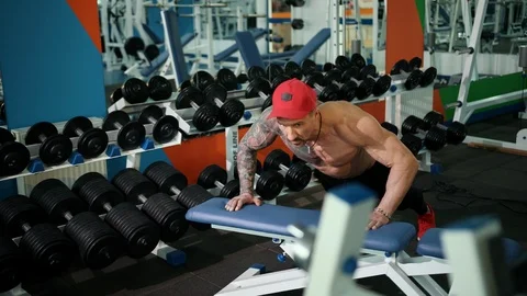 Athletic man in red cap on his head pushes seat off, increasing his muscles. 库存影片 110336689