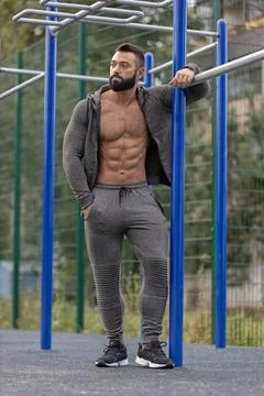 Athletic man resting on a pull up bar in a sports ground during the late Stock Photos