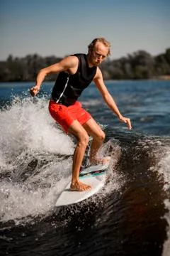 Athletic man rides down the wave on surf style wakeboard on sunny day Stock Photos