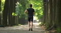 Athletic man run on the beautiful park alley. Real time. Super telephoto lens 4k or 4k+ Resolution