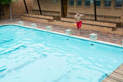 Athletic man running along backyard pool edge holding orange flotation device, Stock Photos