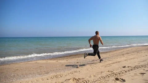 Athletic man running along sandy beach, showcasing dynamic movement and energy Stock Footage 319067709