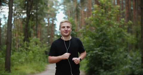 Athletic man running in the Park and doing exercises Jogging while listening to Stock Footage 202145219