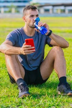 Athletic man sitting on grass drinking water and holding.Vertical Stock Photos
