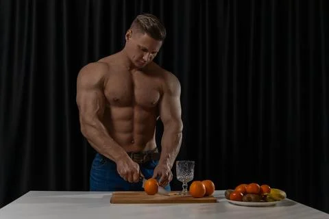 Athletic man skillfully cuts fresh oranges in a modern kitchen while preparing Stock Photos
