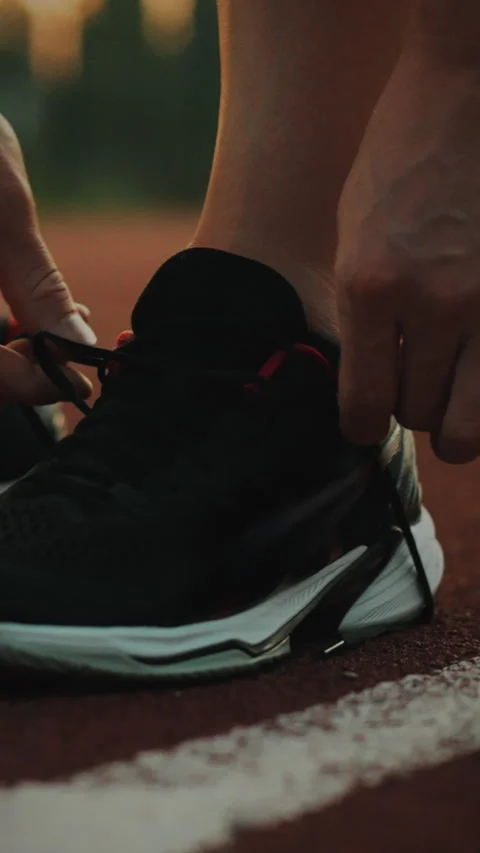 Athletic man ties shoelaces on the playing field during evening practice ses Stock Footage 331535396