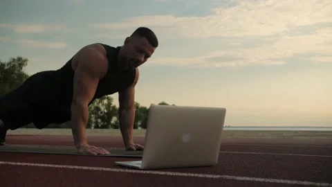 Аthletic man trainer shows his client to do push-ups through the laptop. Stock Footage 200117461