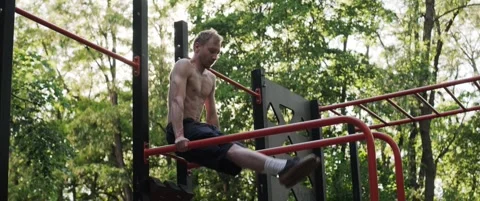 Athletic man training abs on outdoor fitness bars in a park during golden hour Stock Footage 323934295