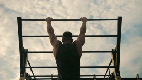 Athletic man is training outdoor, doing pull-ups on his back muscles. Agains Stock Footage 200117569