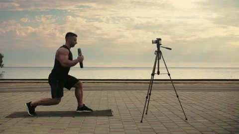 Athletic man training outdoors, recording online classes, doing lunges with  Stock Footage 200117867