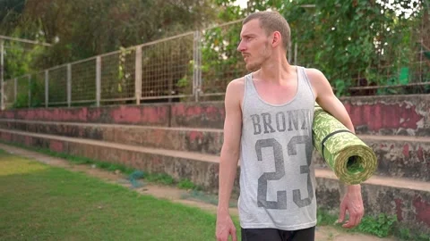 An athletic man walks through the stadium, with a yoga mat under his arm. Video stock 231337083
