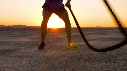 Athletic man working out with battle ropes on a dry lake at sunset Video stock 219885738