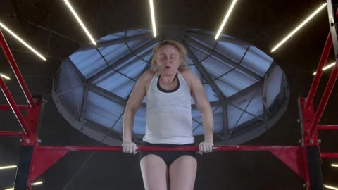 Athletic mature woman doing a pull-up an upper-body strength exercise modern gym Stock Footage 148767565