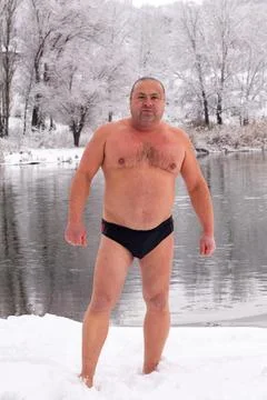 An athletic middle-aged man stands after swimming by an icy river in a snowy Stock Photos