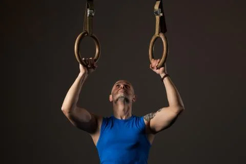 Athletic middle aged man training with rings, studio background Stock Photos
