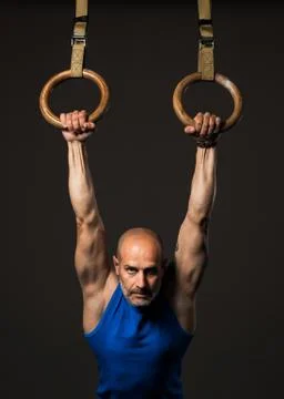 Athletic middle aged man training with rings, studio background Stock Photos
