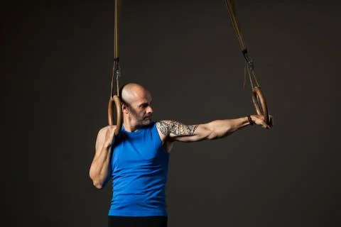 Athletic middle aged man training with rings, studio background Stock Photos