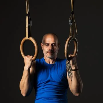 Athletic middle aged man training with rings, studio background Stock Photos