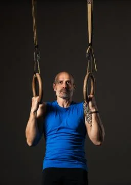 Athletic middle aged man training with rings, studio background Stock Photos
