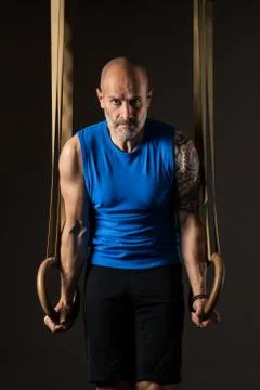 Athletic middle aged man training with rings, studio background Stock Photos