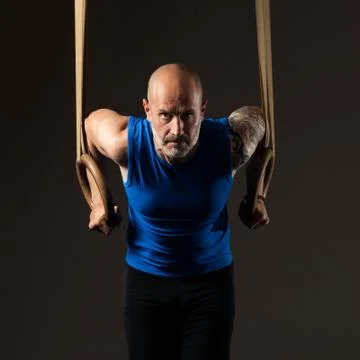 Athletic middle aged man training with rings, studio background Stock Photos
