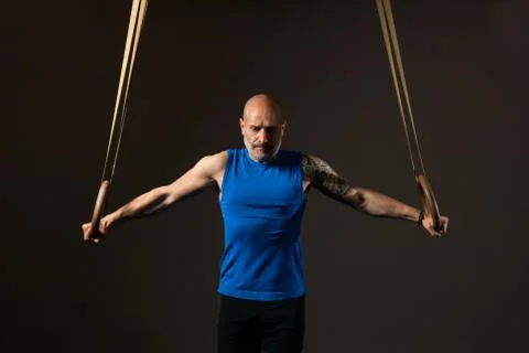 Athletic middle aged man training with rings, studio background Stock Photos