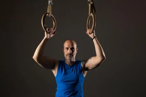 Athletic middle aged man training with rings, studio background Stock Photos