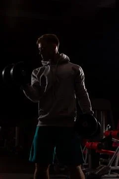 Athletic person performs bicep curls with dumbbells in gym setting during Stock Photos