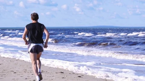 Athletic running man move away along the seethe sea shore Stock Footage 82412893