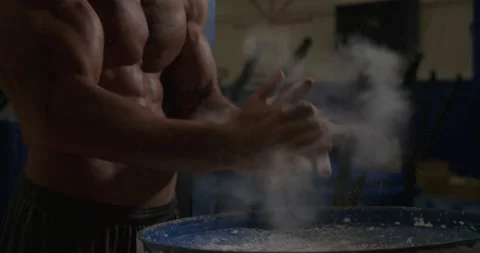 Athletic shirtless man claps hands together with chalk for gymnast rings Video stock 132207656
