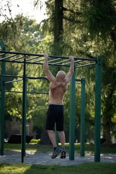 Athletic shirtless man doing pull ups on bars at an outdoor street gym park Stock Photos
