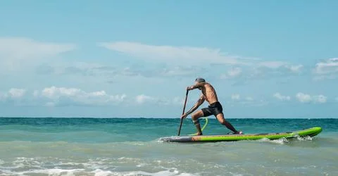 Athletic wiry surfer guy swims with a paddle on a sapboard in the sea Stock Photos