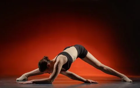 Athletic woman doing side split stretch in studio on red background copyspace Stock Photos