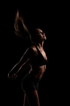 Athletic woman in motion captured in dramatic lighting on black backdrop Stock Photos