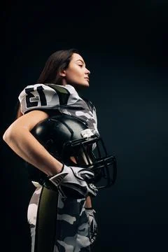 Athletic woman poses in American football uniform with helmet in her hand. Stock Photos