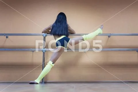 Athletic woman standing near barre in fitness center putting her leg high on Stock Photos