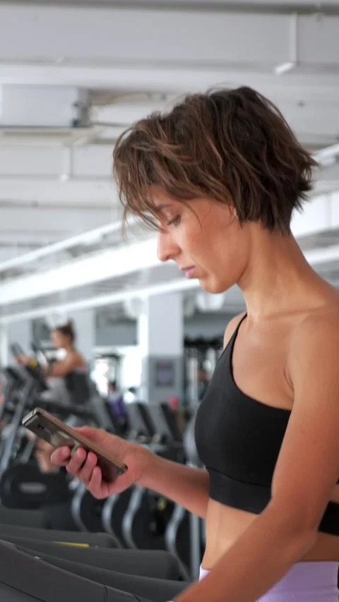 Athletic woman using smartphone while running on treadmill Stock-Footage 341445033