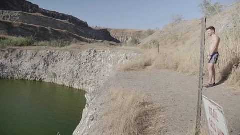 Athletic young guy jumping Into pond from a rock cliff . Stock Footage 116056935