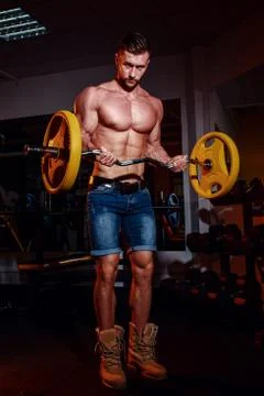 Athletic young man doing exercises with barbell in gym. Handsome muscular bod Stock Photos