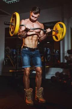 Athletic young man doing exercises with barbell in gym. Handsome muscular bod Stock Photos