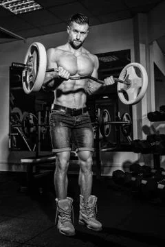 Athletic young man doing exercises with barbell in gym. Handsome muscular bod Stock Photos