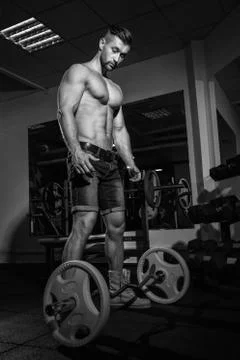Athletic young man doing exercises with barbell in gym. Handsome muscular bod Stock Photos
