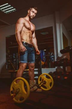 Athletic young man doing exercises with barbell in gym. Handsome muscular bod Stock Photos