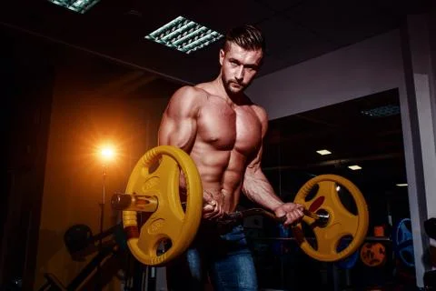 Athletic young man doing exercises with barbell in gym. Handsome muscular bod Stock Photos
