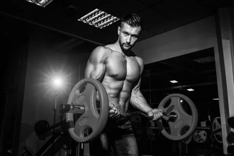 Athletic young man doing exercises with barbell in gym. Handsome muscular bod Stock Photos